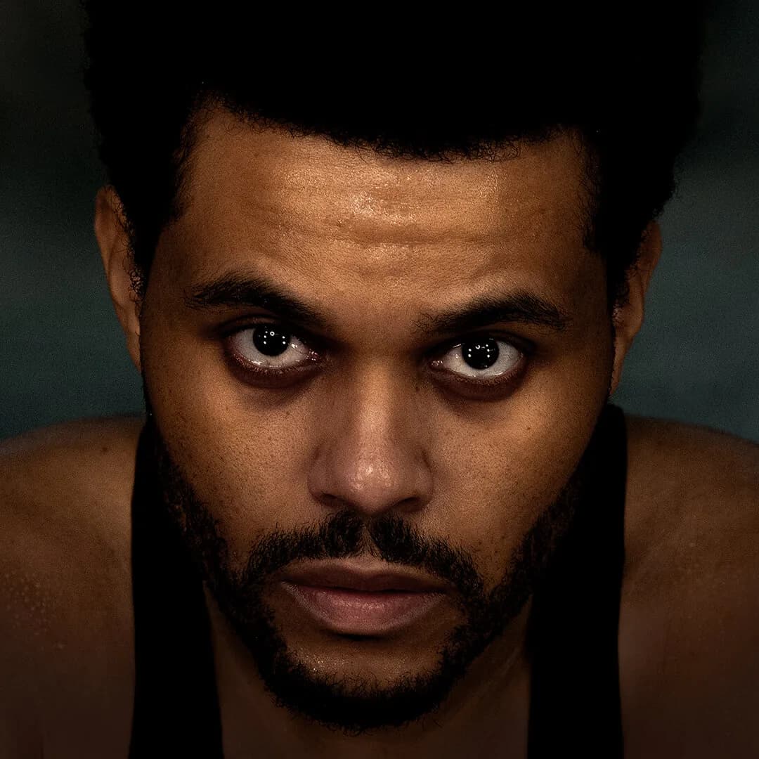 Close-up portrait of The Weeknd in warm low light — official artist photo